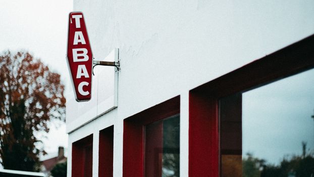 A vintage red 'Tabac' sign outside a white building with red accents, autumn setting.