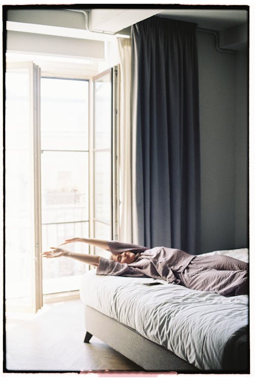 Woman Stretching on Bed near Balcony Door