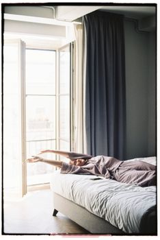 A woman stretching on a bed near an open balcony door with soft, morning sunlight.