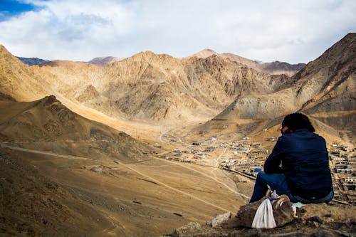 Person Sitting on Mountain Under White Sky