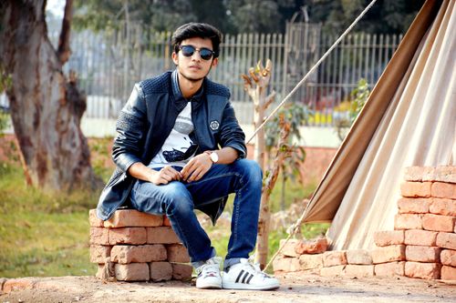 Free A young man in casual wear with sunglasses sits outdoors, expressing a relaxed lifestyle. Stock Photo