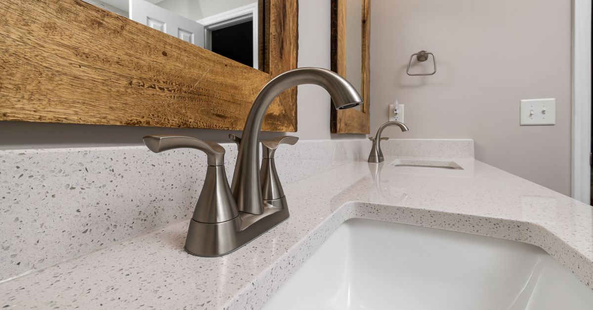 Close-up of a contemporary bathroom sink with a sleek faucet and wooden mirror frame