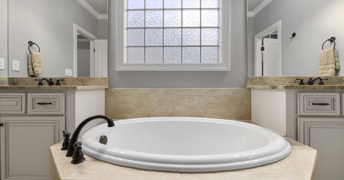 A luxurious bathroom featuring a marble bathtub, pristine cabinets, and elegant lighting.