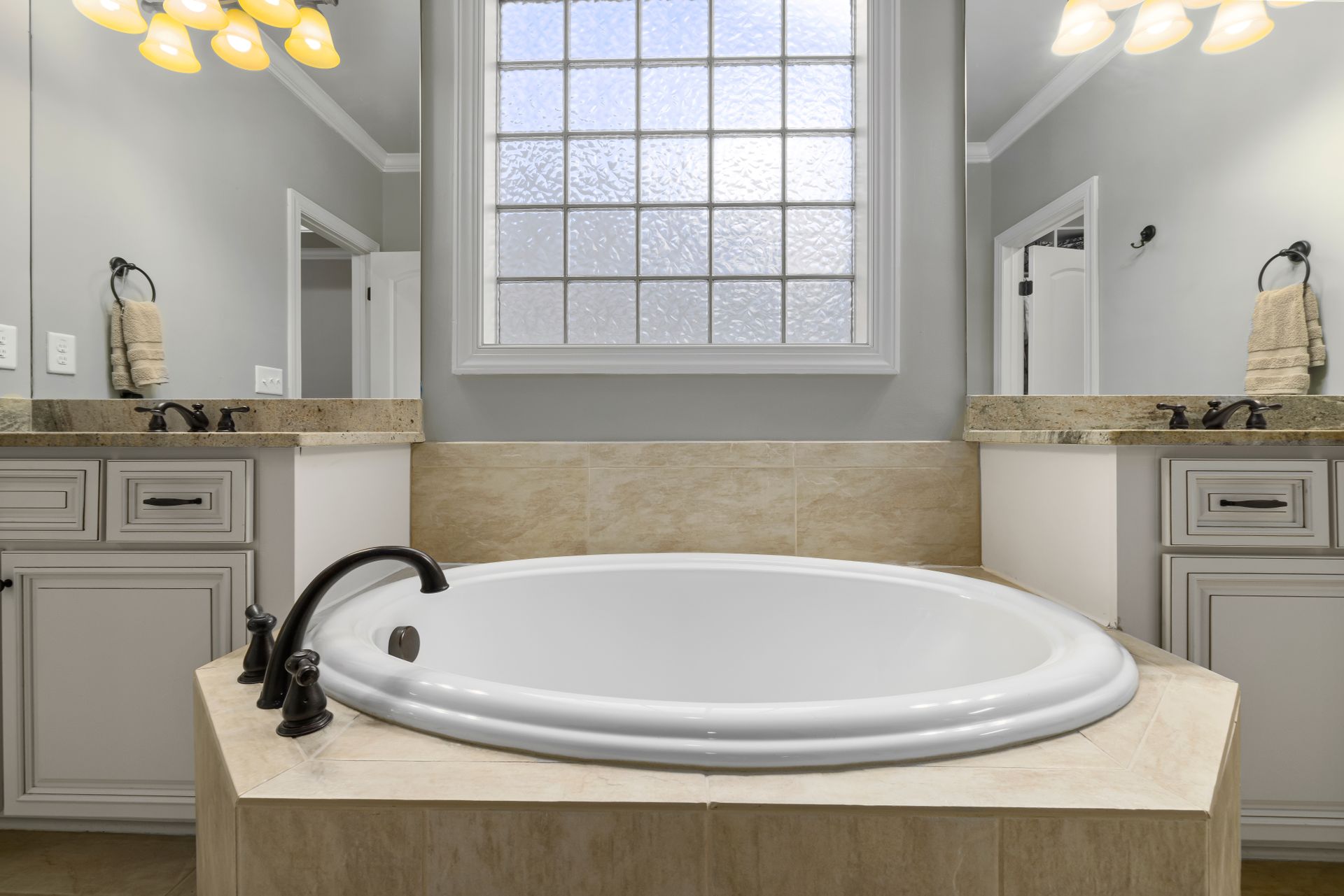 A luxurious bathroom featuring a marble bathtub, pristine cabinets, and elegant lighting.
