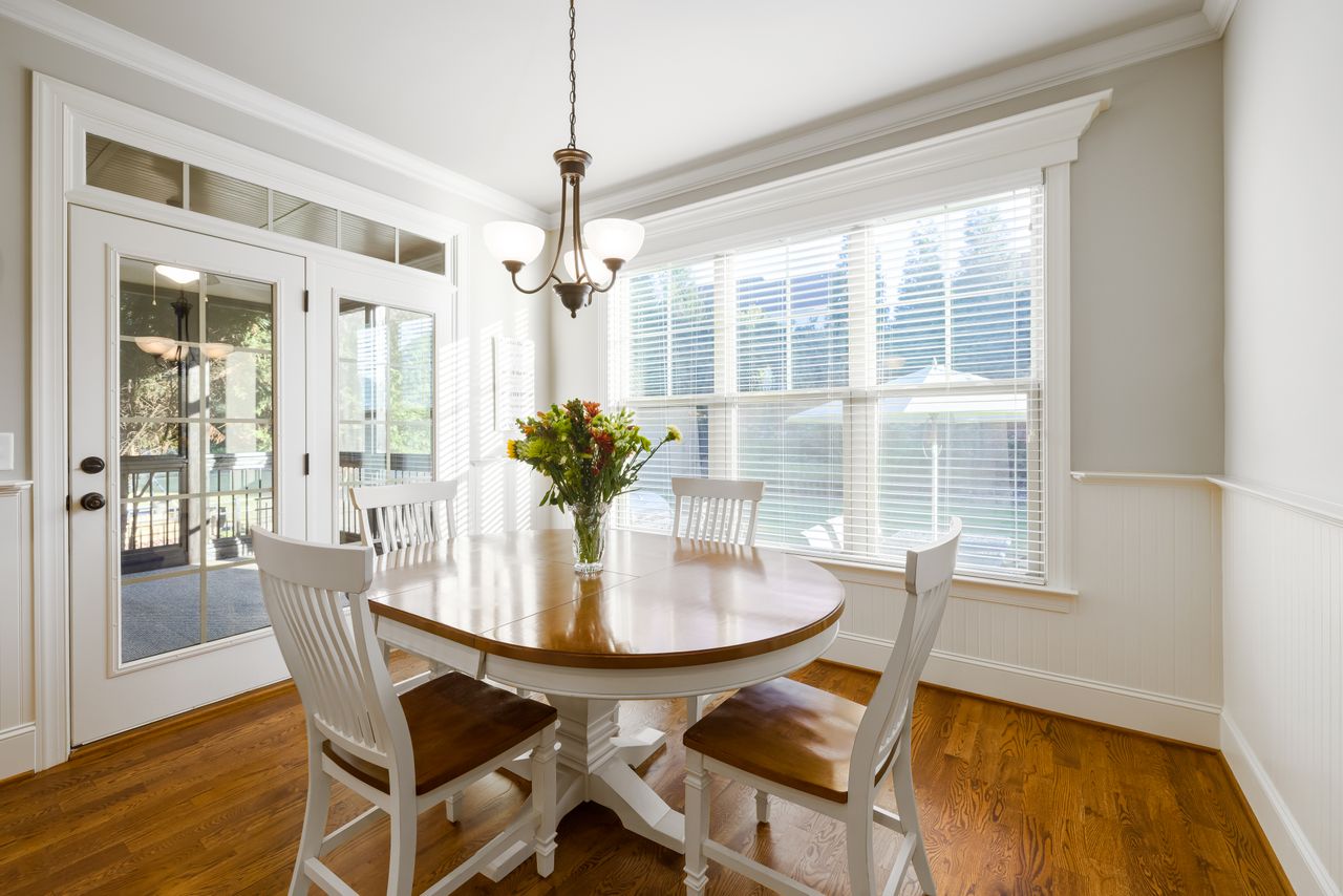 Four white and wood chairs around a round white pedestal table in a bright breakfast nook