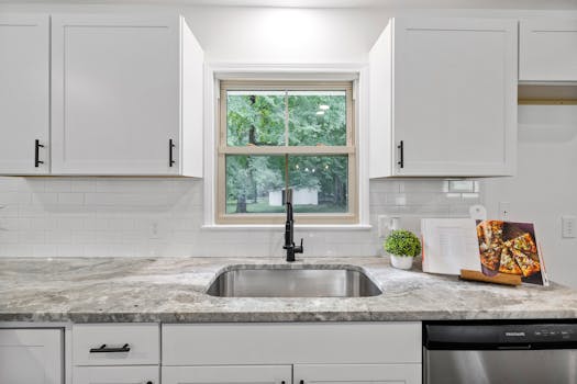 Bright kitchen interior featuring white cabinets, granite countertop, and a window with a view.