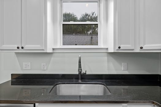Elegant kitchen interior highlighting a sleek sink, black countertop, and white cabinets under natural light.
