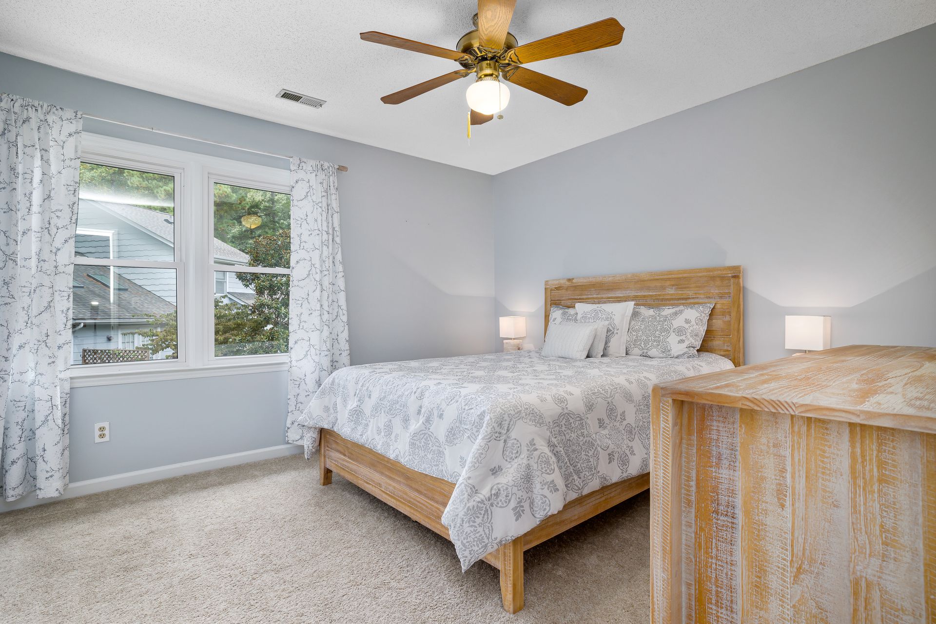 Bright and airy bedroom with wooden furniture and a ceiling fan, exuding a cozy and modern feel.