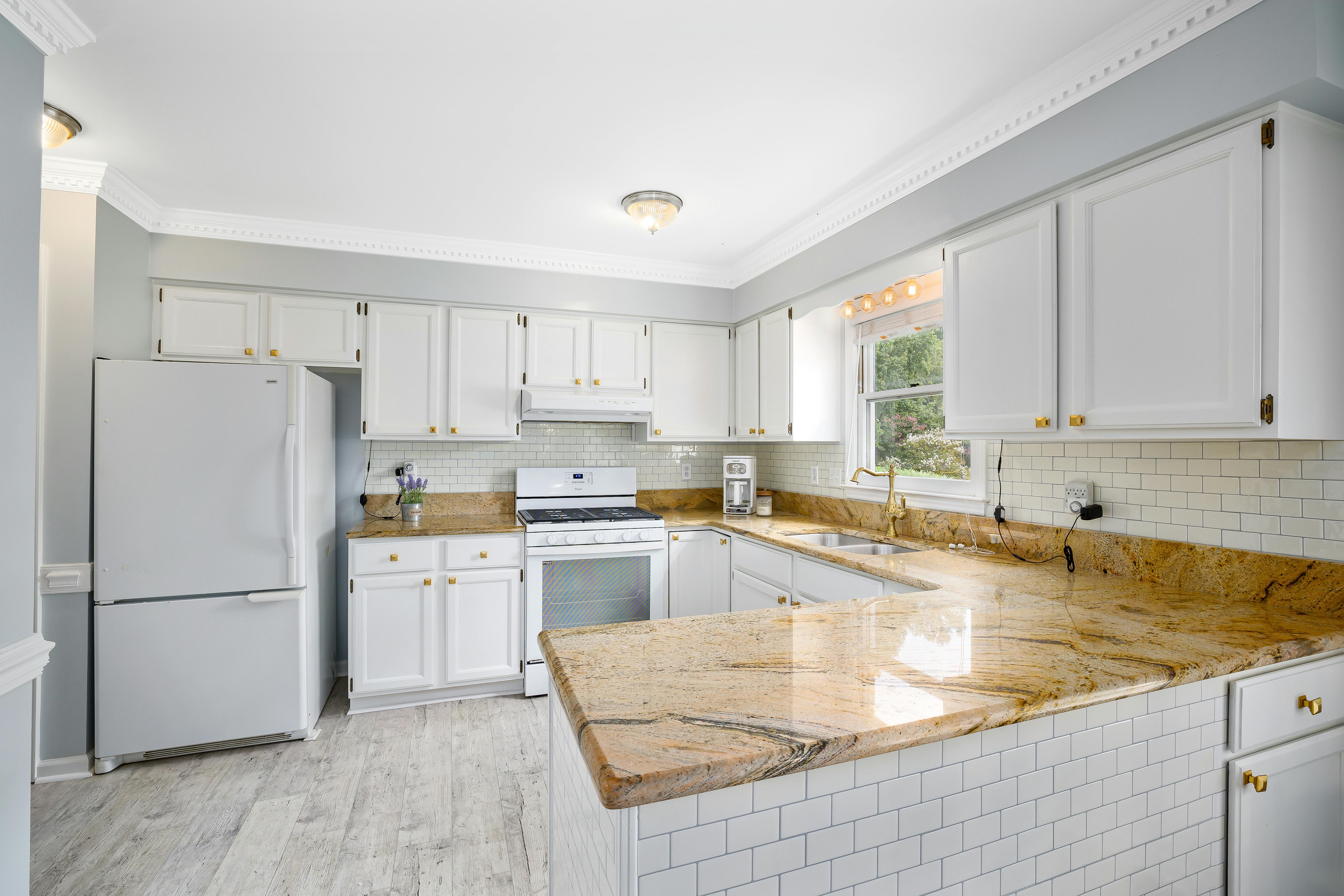 A bright kitchen with white cabinets, marble countertops, and modern appliances.