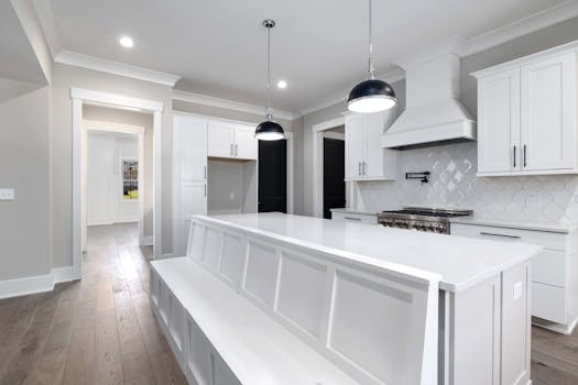 Sleek white kitchen with modern furniture and elegant lighting fixtures.