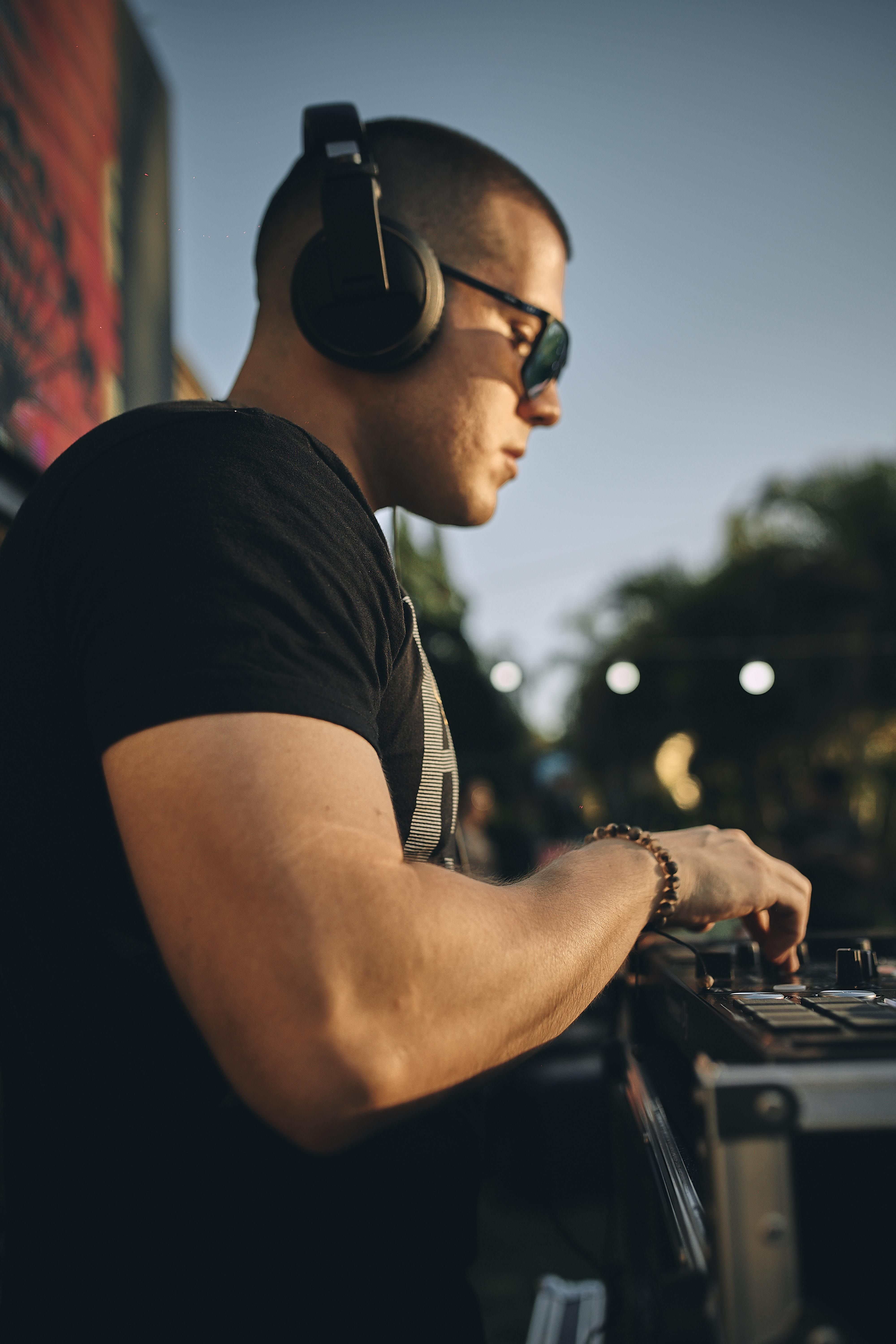 A DJ playing music with headphones at an outdoor festival during the day.