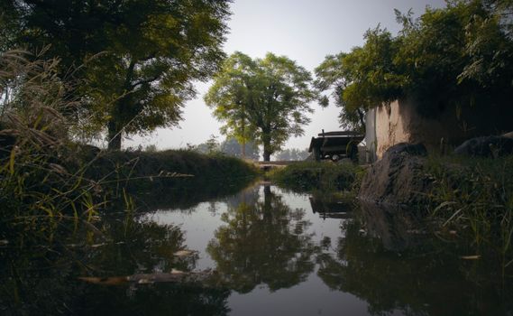 Scenic rural landscape featuring a reflective waterway, lush green trees, and rustic charm.