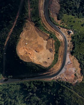 Aerial shot showcasing a winding road next to a quarry amidst lush greenery.