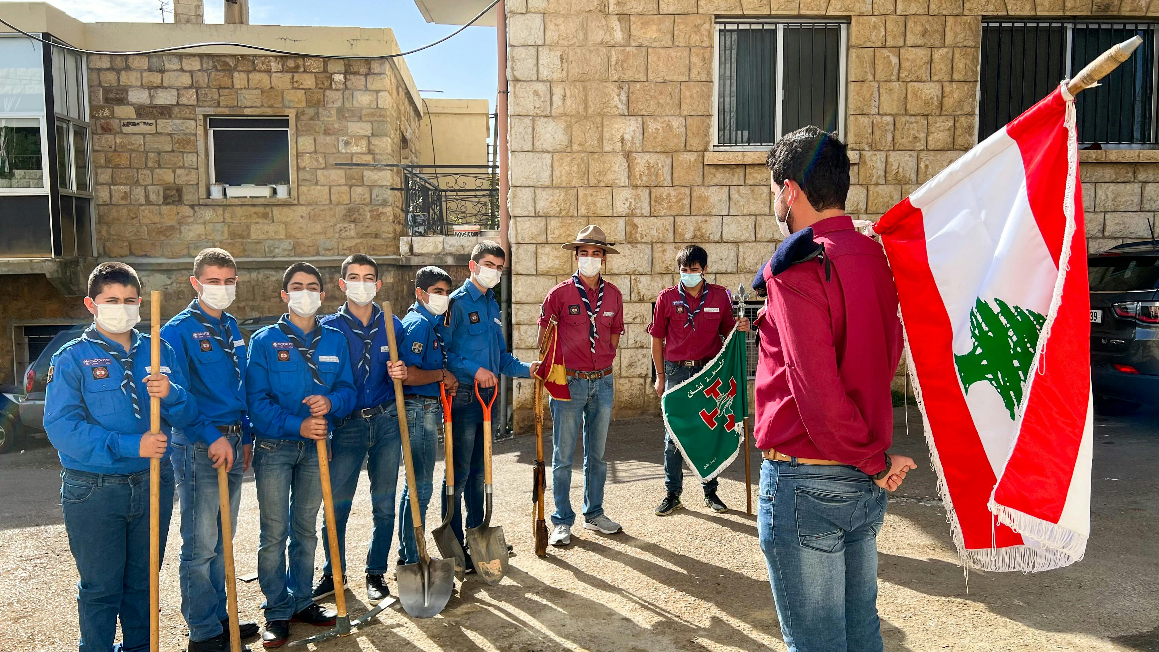 Group of scouts in uniforms holding shovels and flags outdoors in Lebanon.