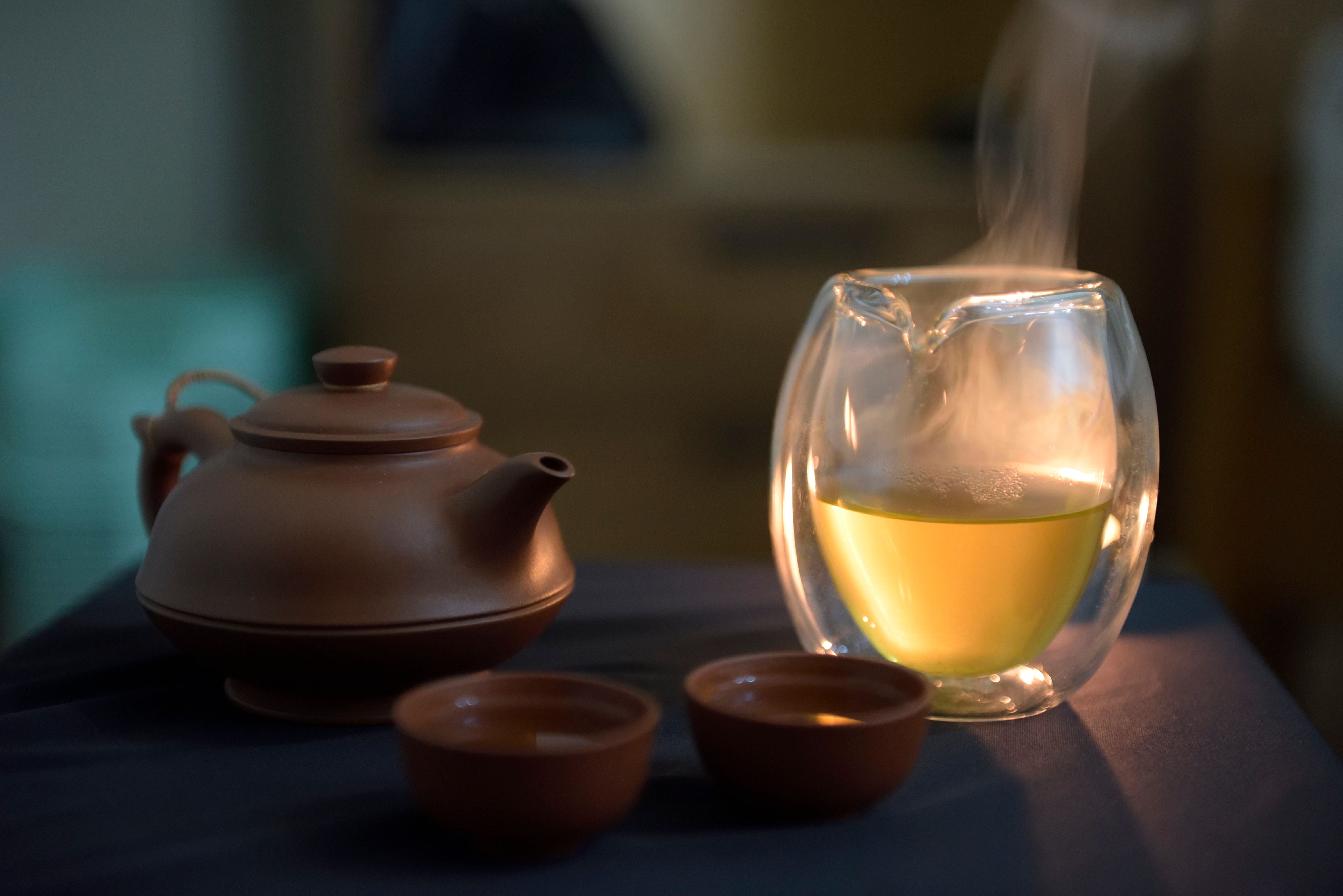 A warm setup featuring a pottery teapot with steaming glass of tea.