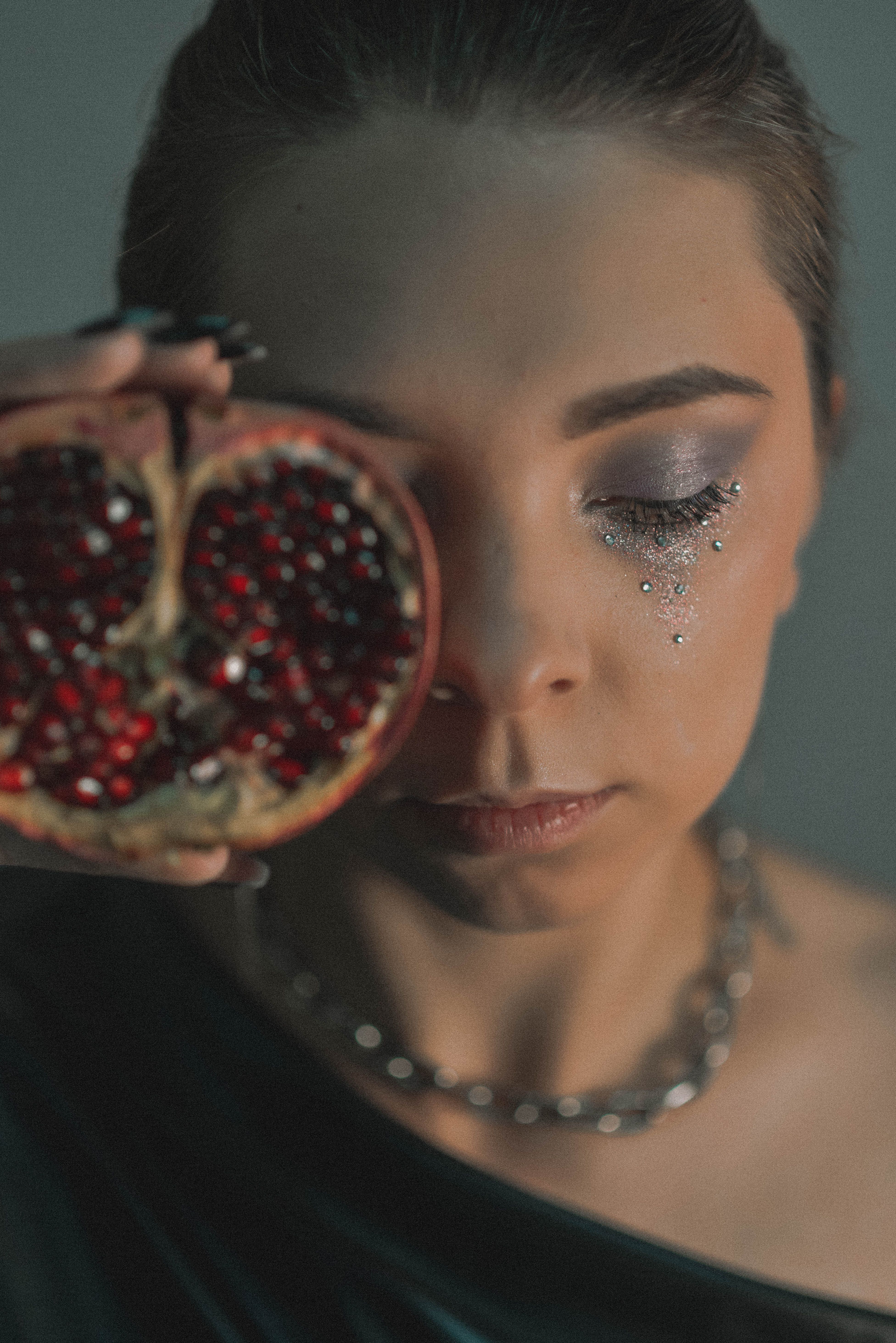Artistic portrait of a woman holding pomegranate with creative eye makeup, indoors.