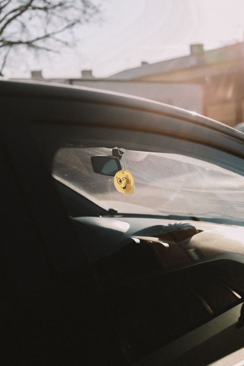 Free A car's interior with a view through the window featuring a yellow hanging ornament. Sunlight creates a warm atmosphere. Stock Photo