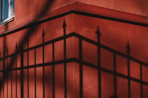 Free Artistic shadow of iron fence cast on a vibrant red building corner, highlighting the interplay of light and architecture. Stock Photo