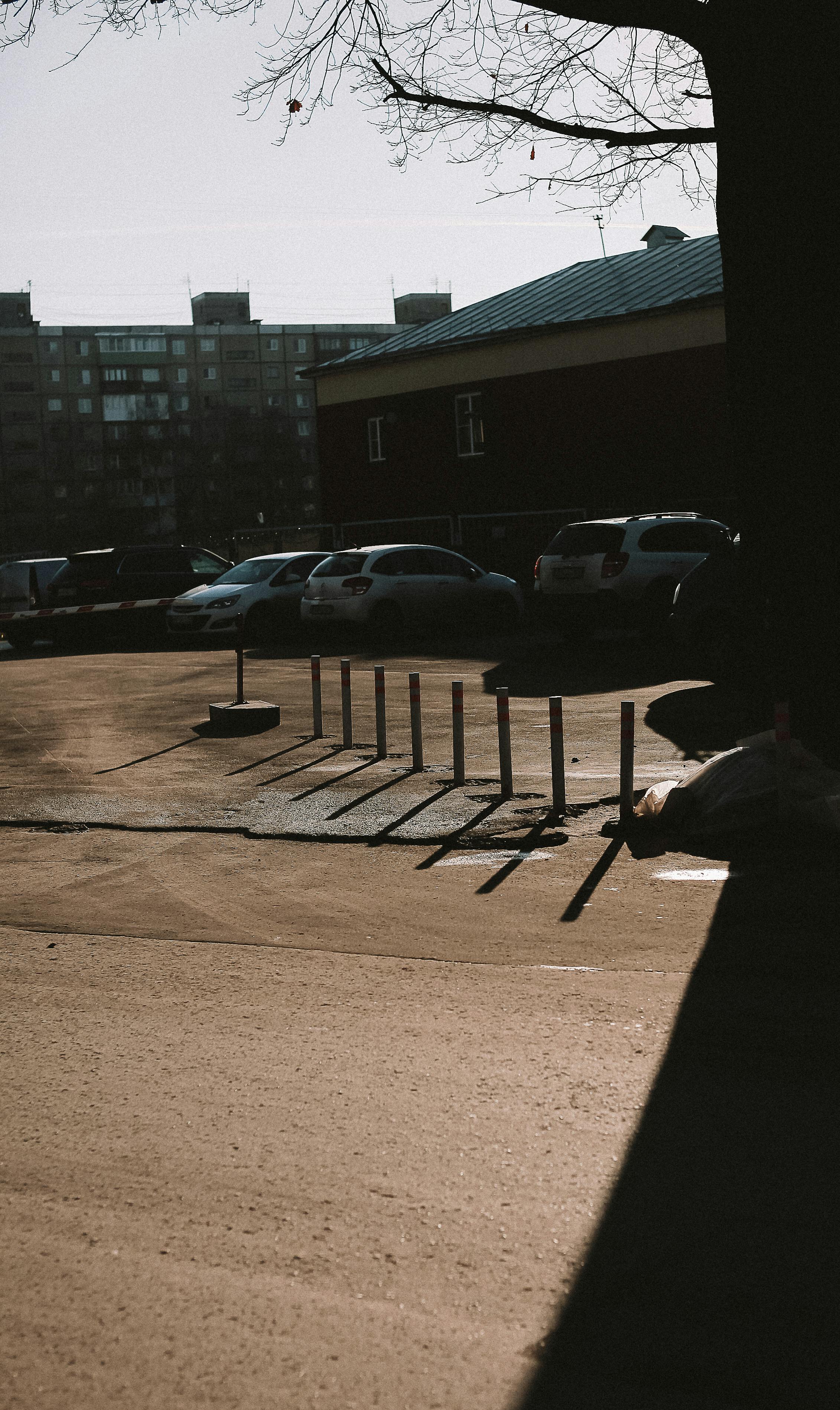 City parking lot with parked cars, shadows, and buildings in the background.