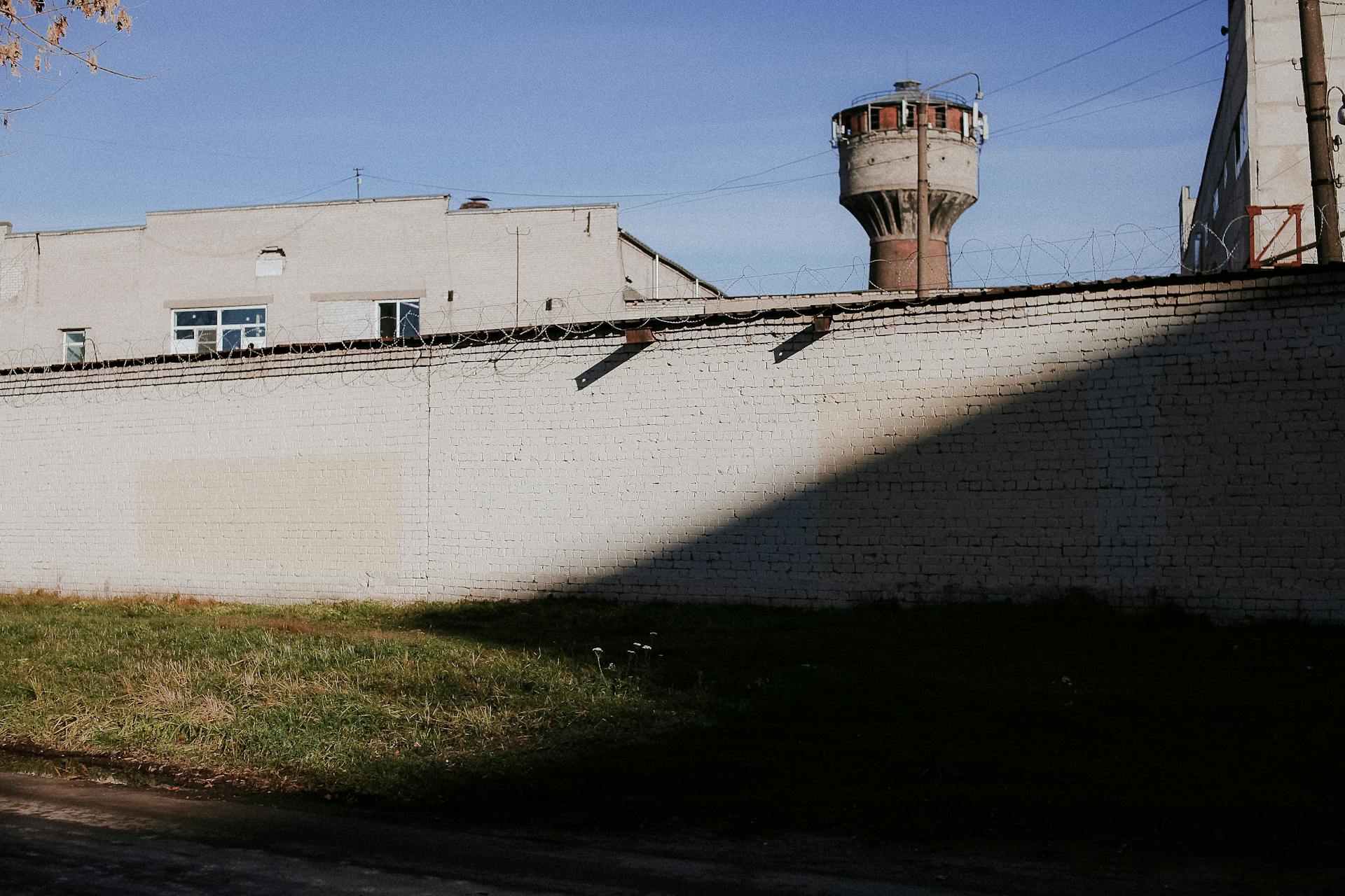 Brick wall with barbed wire and a lookout tower under a clear blue sky, suggesting security and protection.