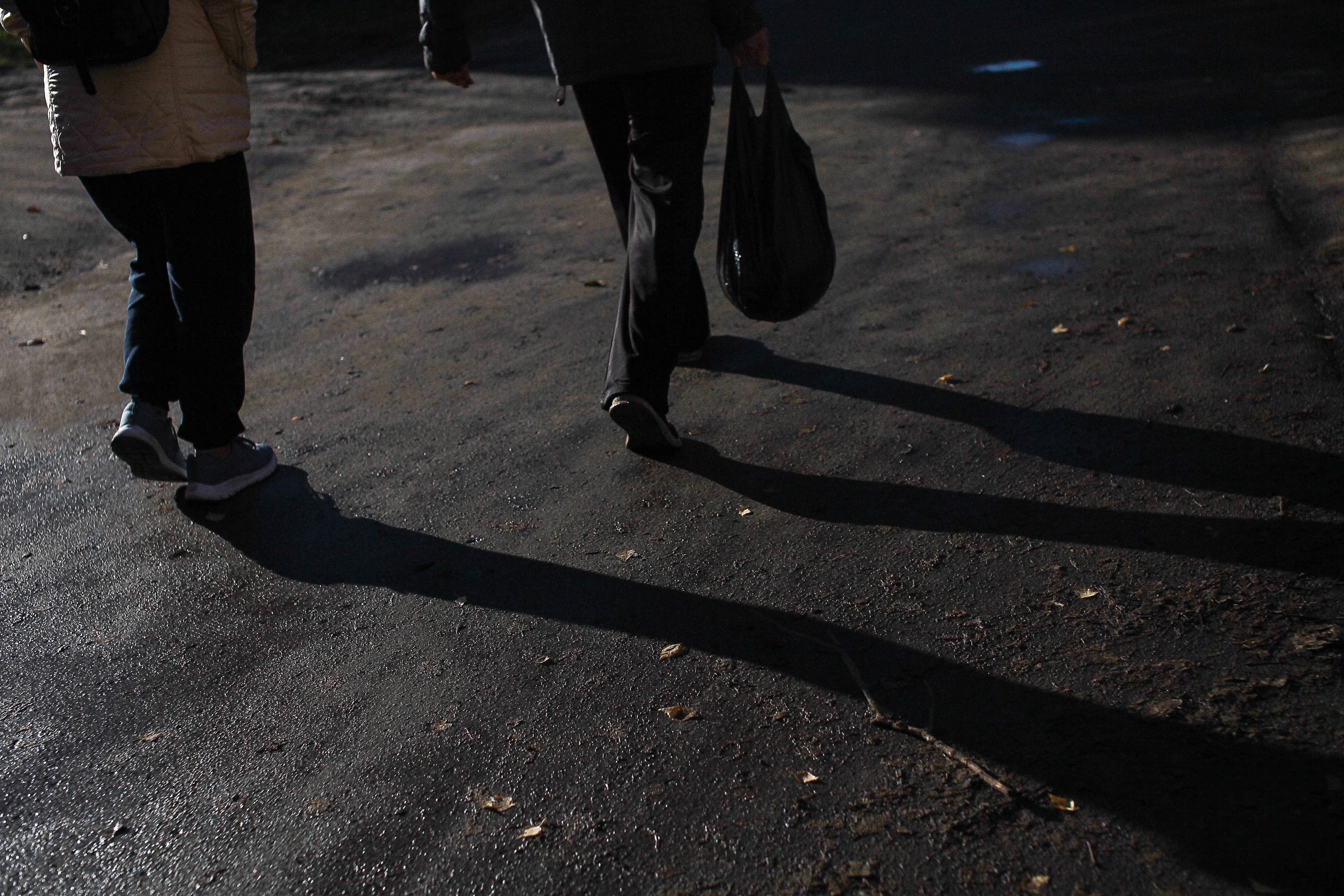 Capture of two people walking, casting long shadows on a paved path.