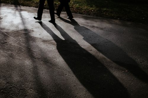 Free Two individuals walking on a wet road casting long shadows at twilight. Stock Photo