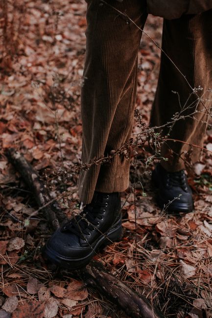 Close-up of black leather shoes on brown corduroy pants in a forest during fall.