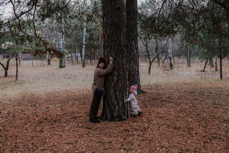 Woman In Brown Jacket And A Baby Hugging The Tree Trunk 