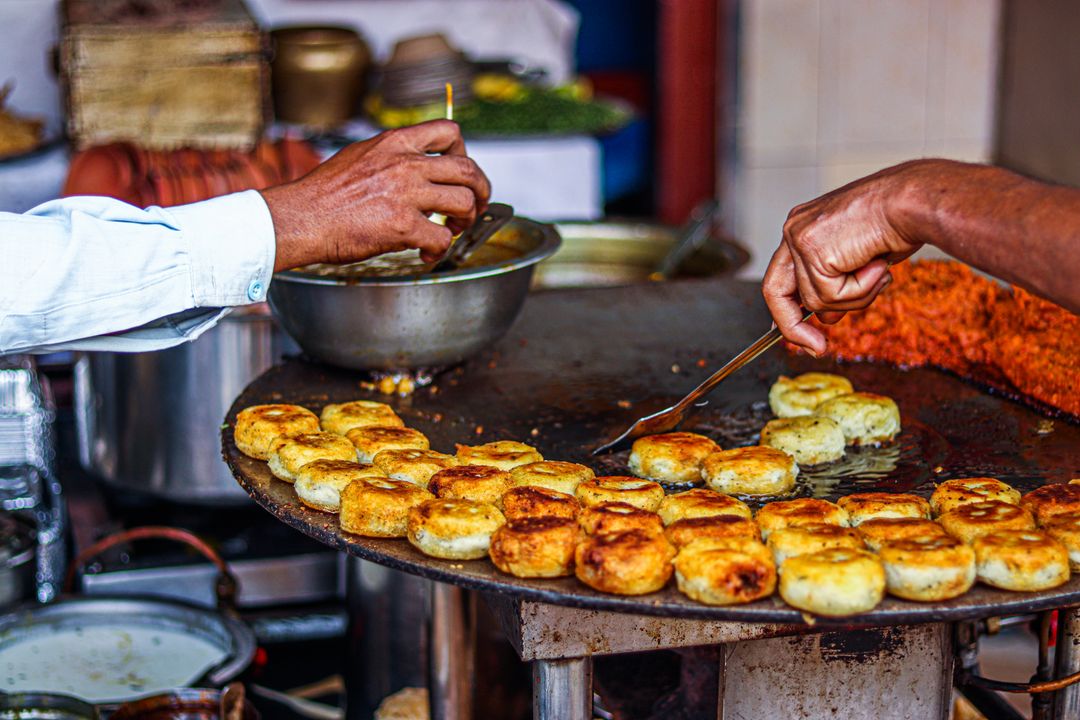 Navratri Catering for Garba Events: How to Land Your First Contract in Ahmedabad 2 Hands frying golden aloo tikki patties on a large flat griddle at a street food stall