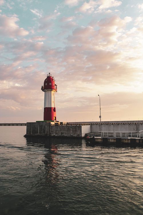 Free A tranquil sunset over a red and white lighthouse by the ocean, perfect for coastal themes. Stock Photo