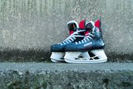 Pair of black and red ice hockey skates placed outdoors on a concrete surface.