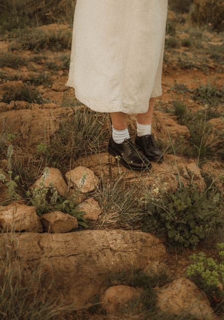 Close-up of a woman's feet in vintage shoes standing on a rocky path surrounded by grass.