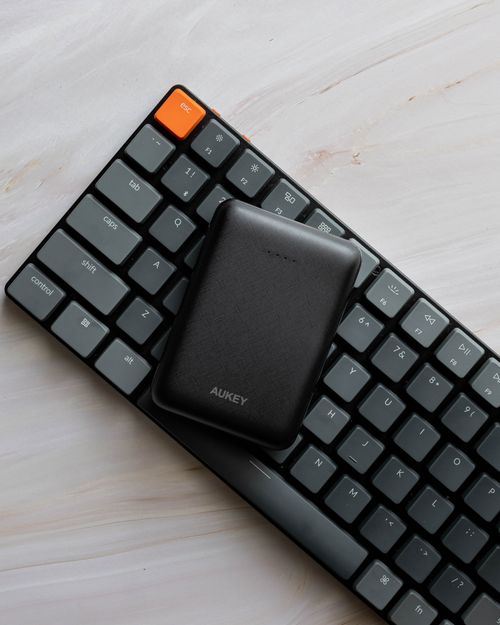 Free Top view of a minimalist mechanical keyboard with a compact power bank on a light wooden surface. Stock Photo