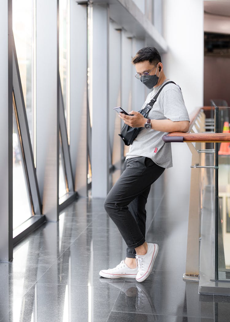 Man Wearing A Facemask Using His Smartphone While Leaning Against The Railings