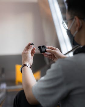 A man using wireless earphones while sitting indoors in a modern environment.