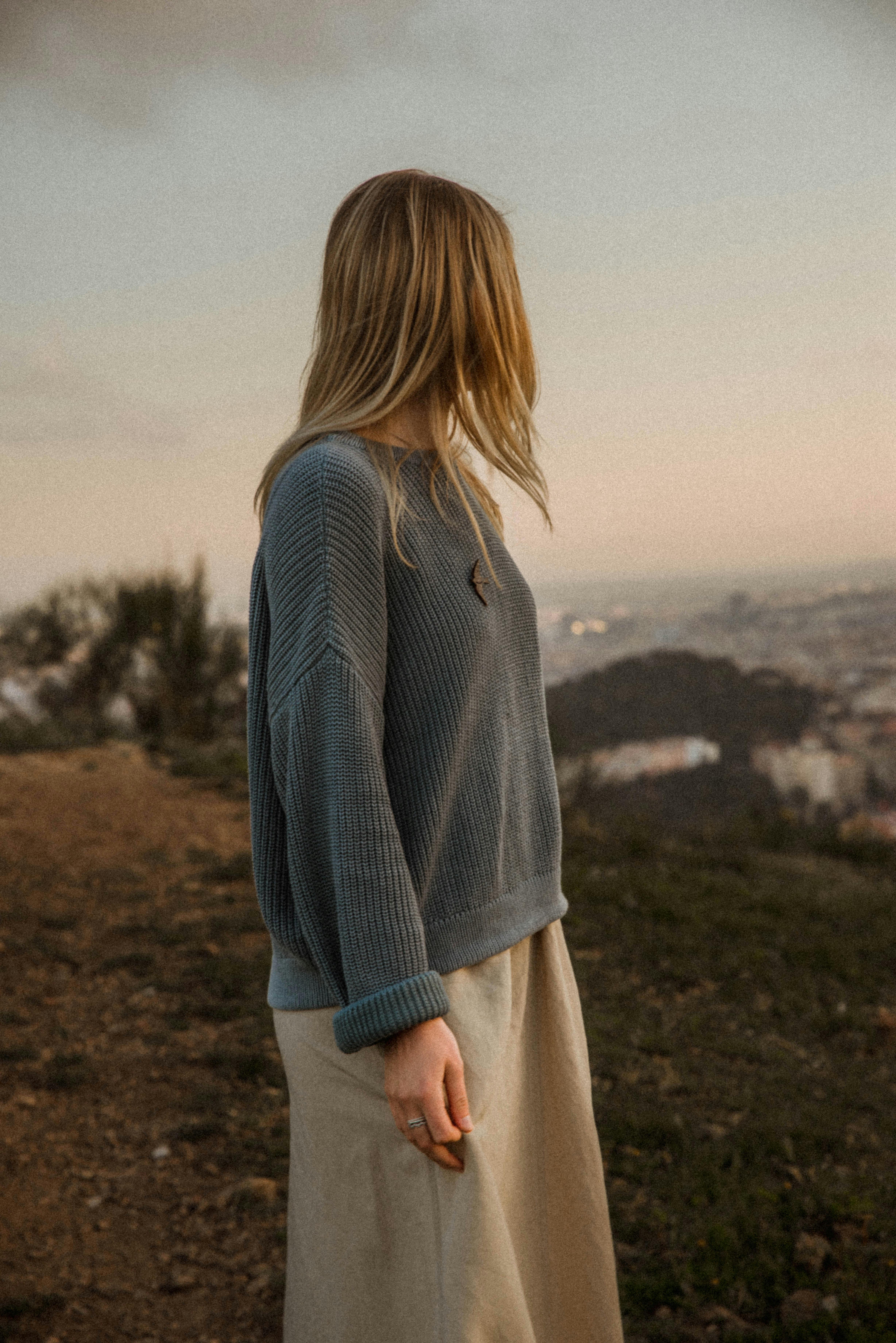 A woman in a gray sweater looks out at a scenic view during sunset.