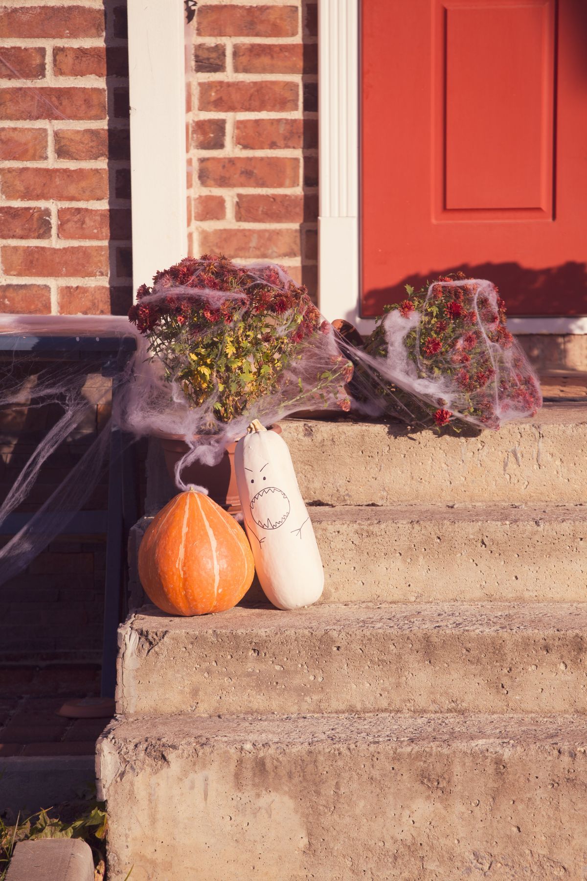 Festive Halloween porch with pumpkins and spider webs beside a red door