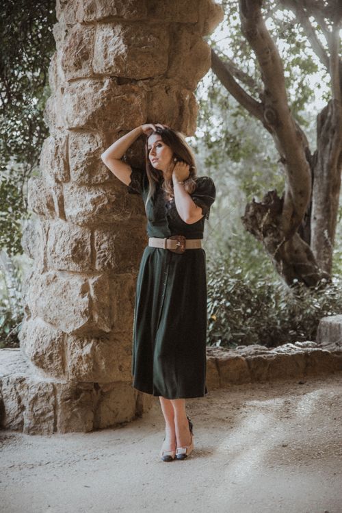 Free A woman in a vintage black dress poses by a stone pillar in a serene outdoor setting. Stock Photo