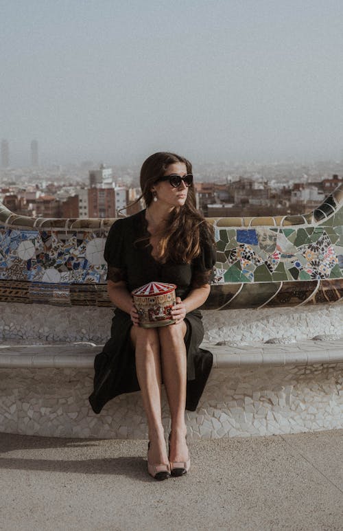 Photo of a Woman in a Black Dress Sitting on a Concrete Surface