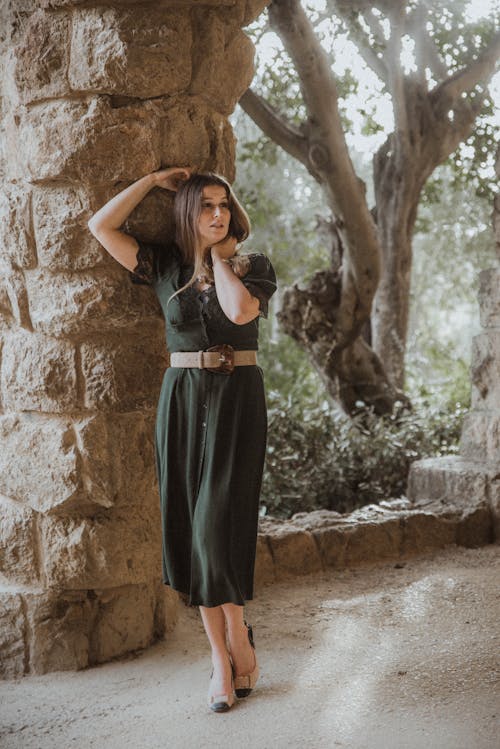 A Woman in Black Sleeveless Dress Standing Beside a Stone Pillar