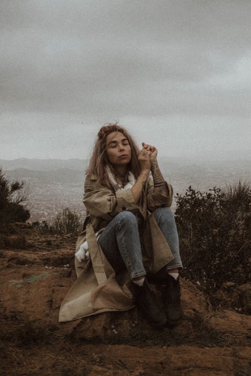 Photograph of a Woman in a Coat Sitting on the Ground