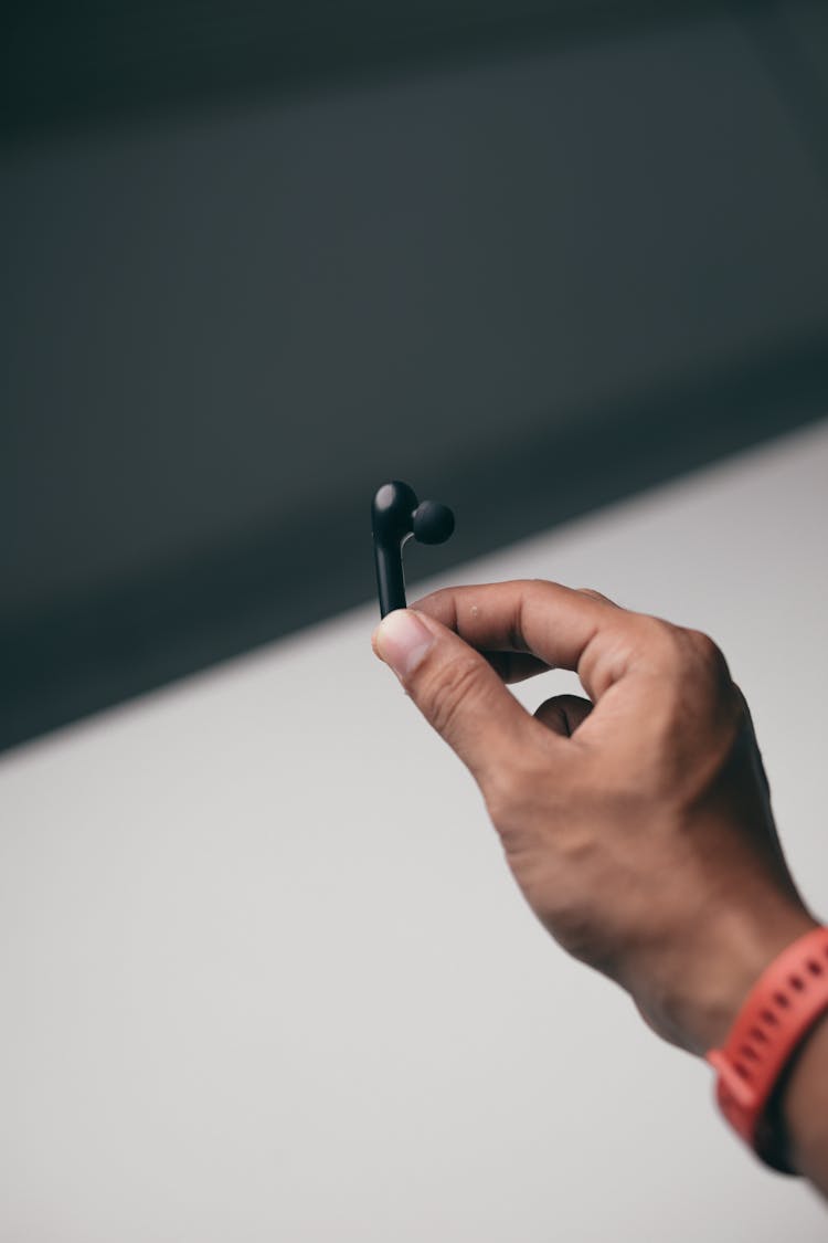 A Man Holding A Piece Of Black Earbud