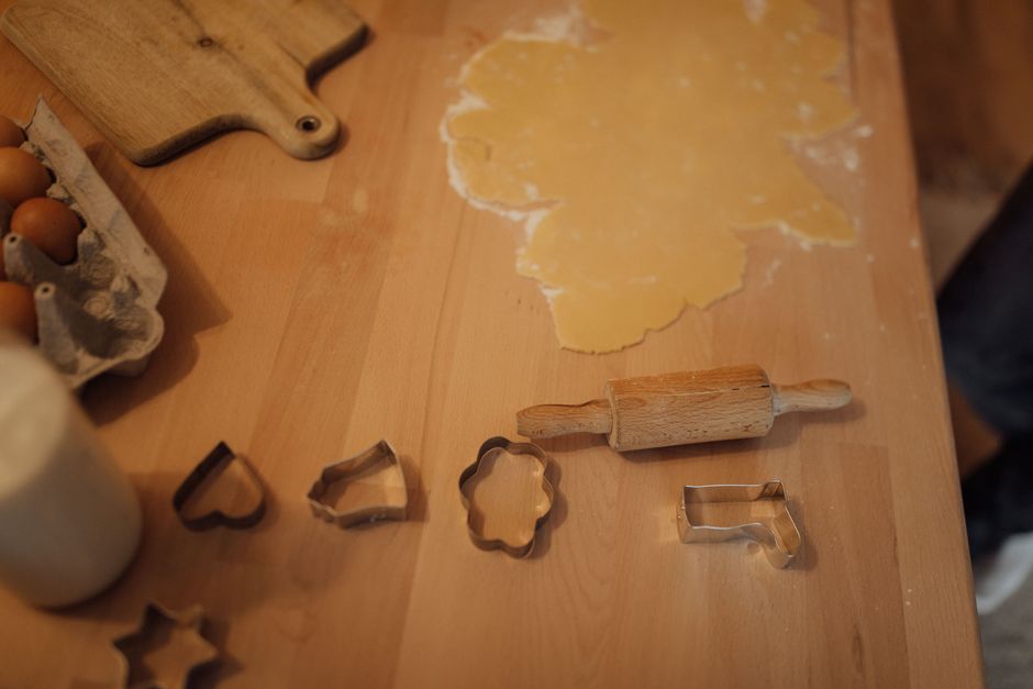 Detailed view of baking preparations with dough, cookie cutters, and eggs on a wooden table.