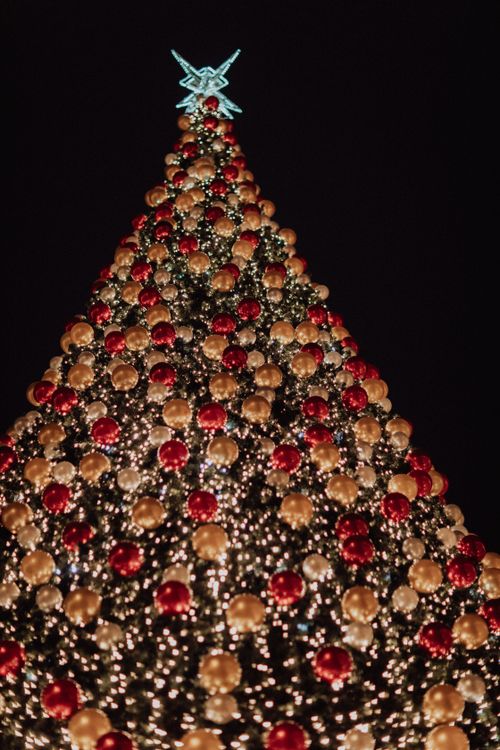 Free Vertical shot of a sparkling Christmas tree with colorful ornaments and lights against a dark night sky. Stock Photo