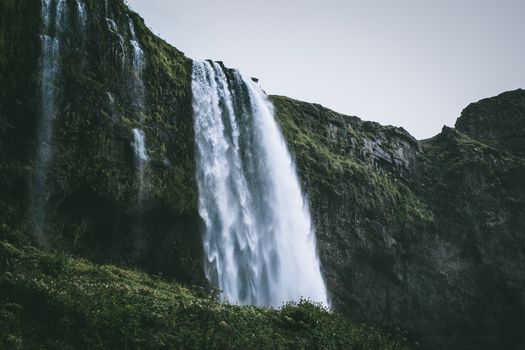 Dramatic waterfall cascading down a lush green cliff in Iceland's stunning natural setting.