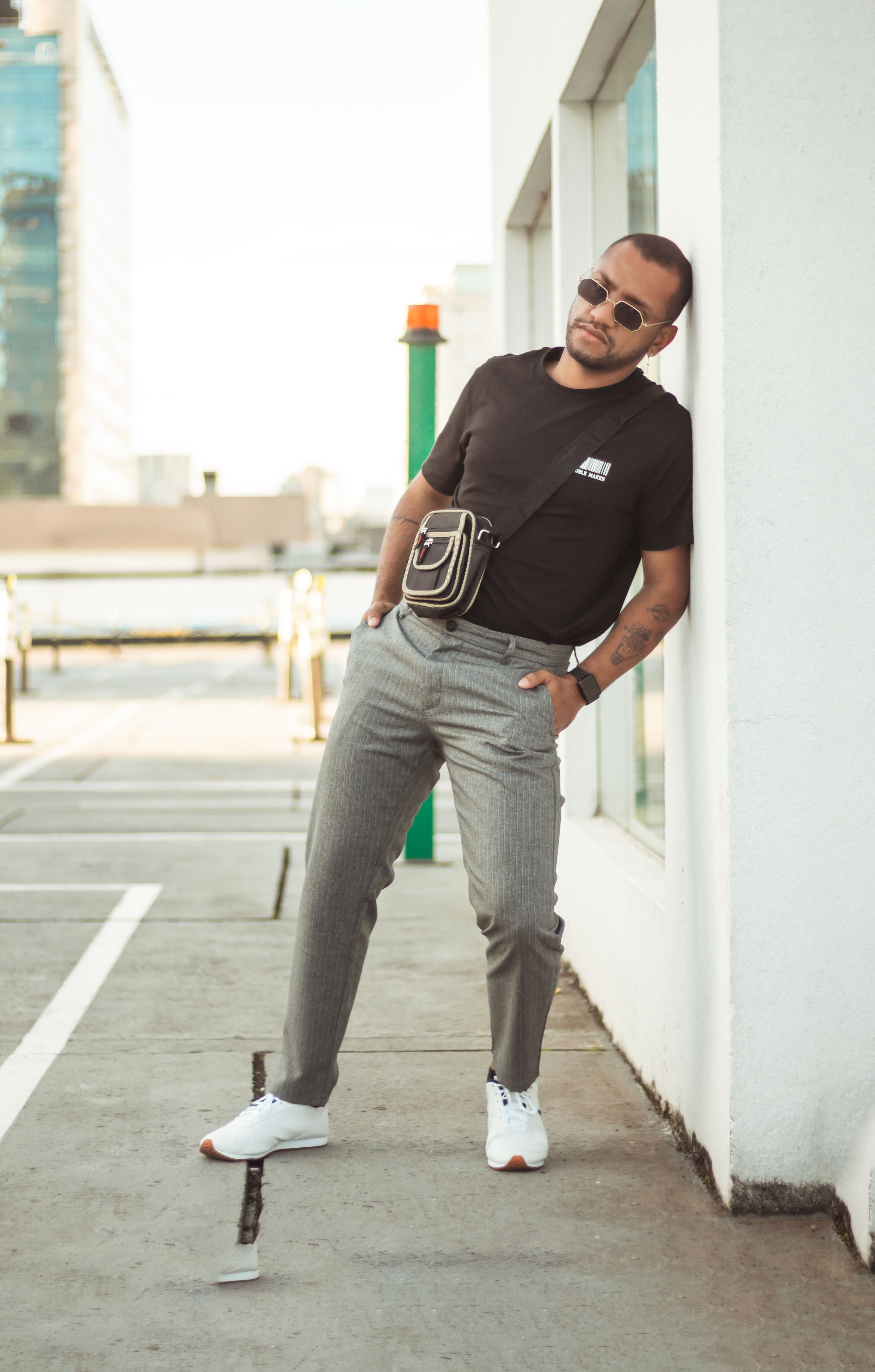 Casual man with sunglasses leans on a city wall in smart casual attire, outdoors.