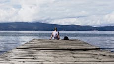一位女子坐在木码头上，欣赏着宁静的湖景和远山