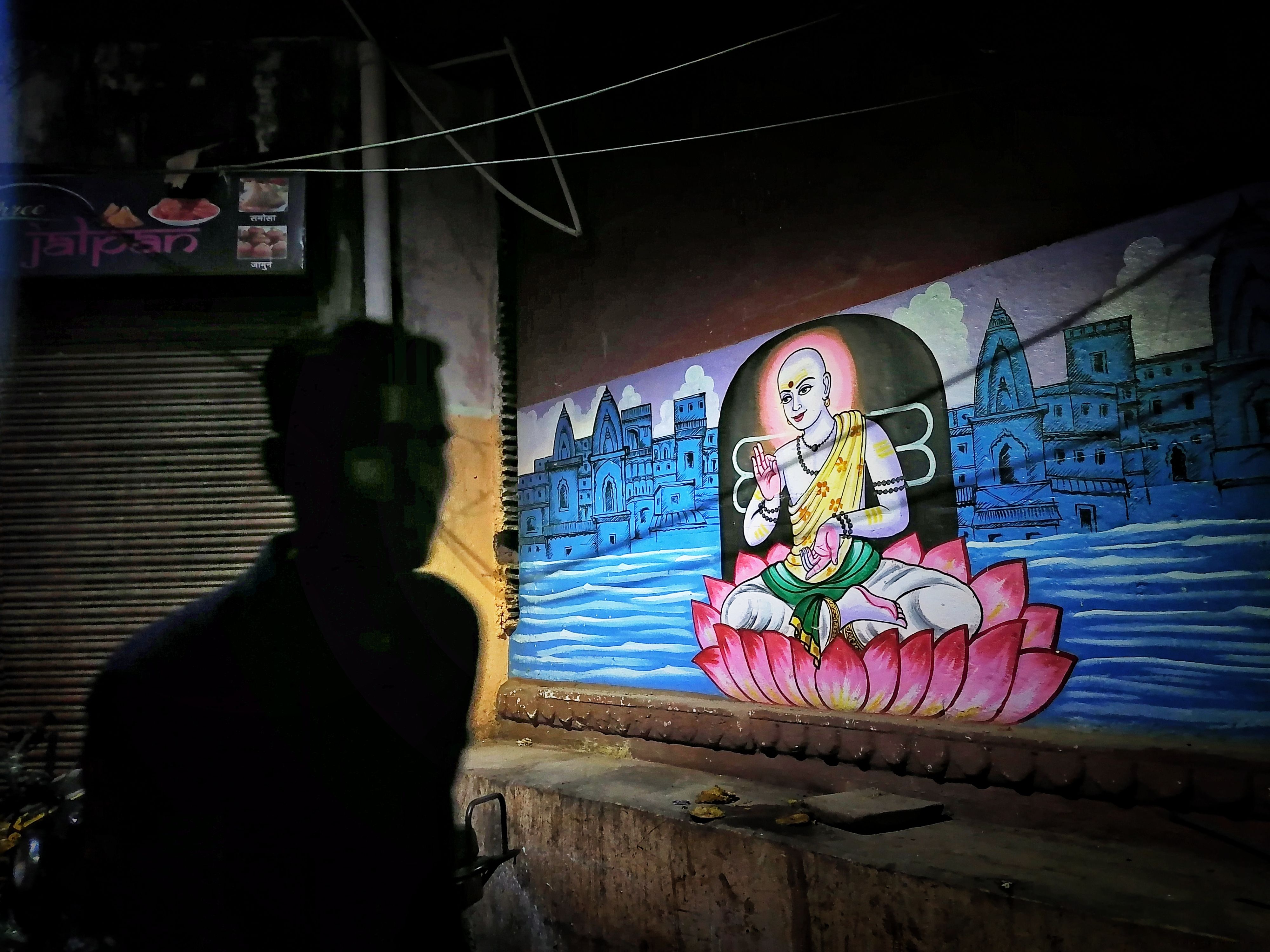 Vivid mural in Varanasi depicting a serene scene with a silhouetted figure in foreground.