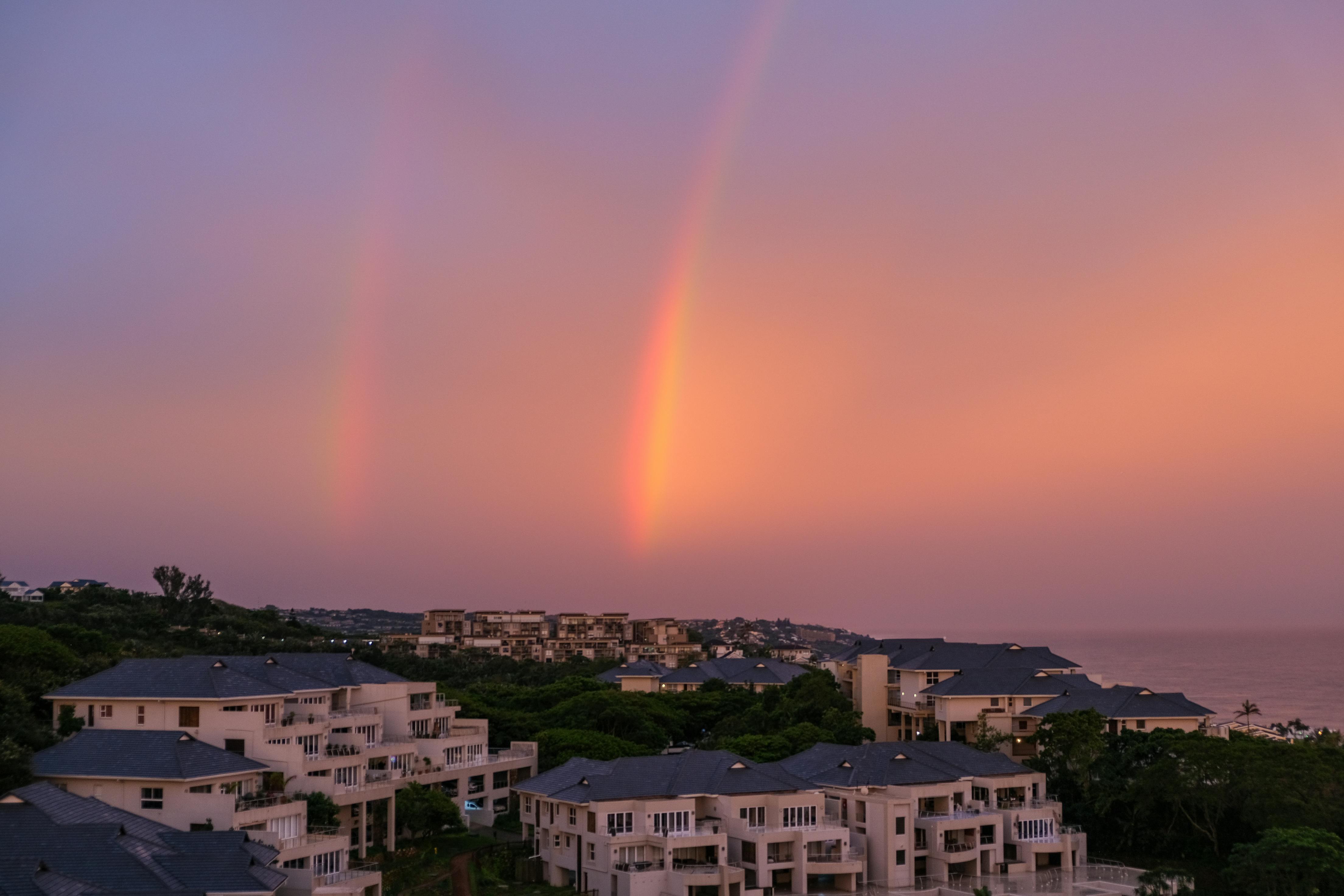 Stunning cityscape with a rainbow against a vivid sunset sky over urban architecture.