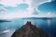 这张航拍照片令人惊叹，捕捉到了圣托里尼岛崎岖的海岸线和宁静的蓝色大海，映衬在充满活力的天空下